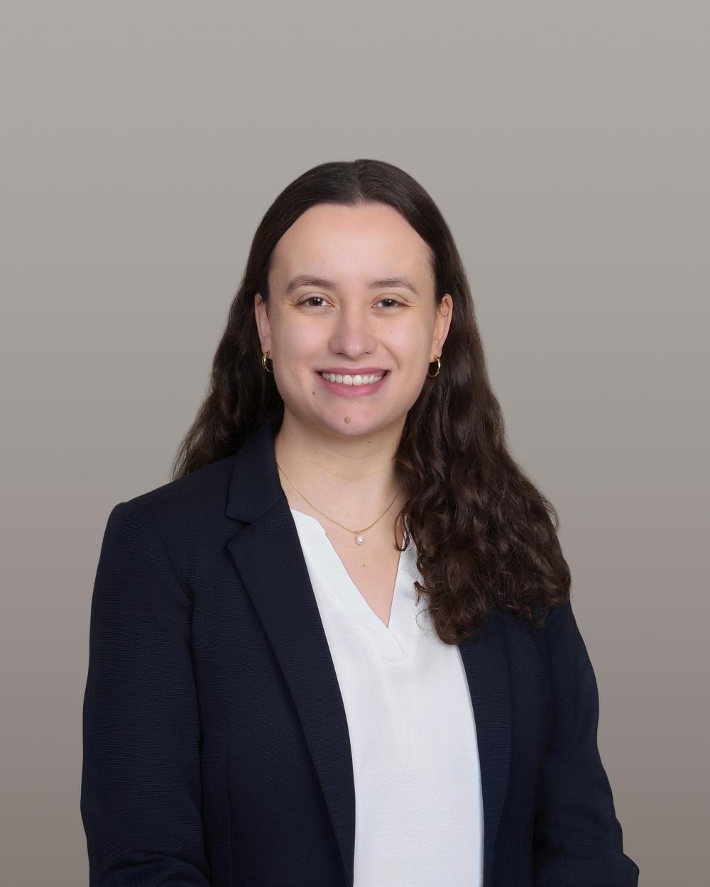 women with wavy brown hair parted down the middle with a white shirt and dark blazer poses for her headshot