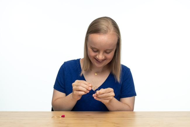 woman with down syndrome with blonde hair that hits her shoulders, handmakes a jewelery item